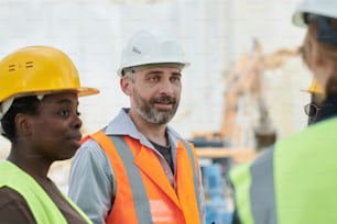 Middle aged confident foreman or manager of team of marble quarry workers talking to subordinates while looking at one of them