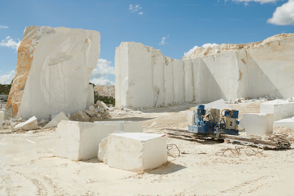 Part of territory of marble quarry surrounded by thick and tall white rock walls and detail of industrial machine on the ground