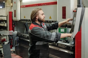 Young male technician in workwear standing in front of control terminal and choosing adjustment points while touching screen