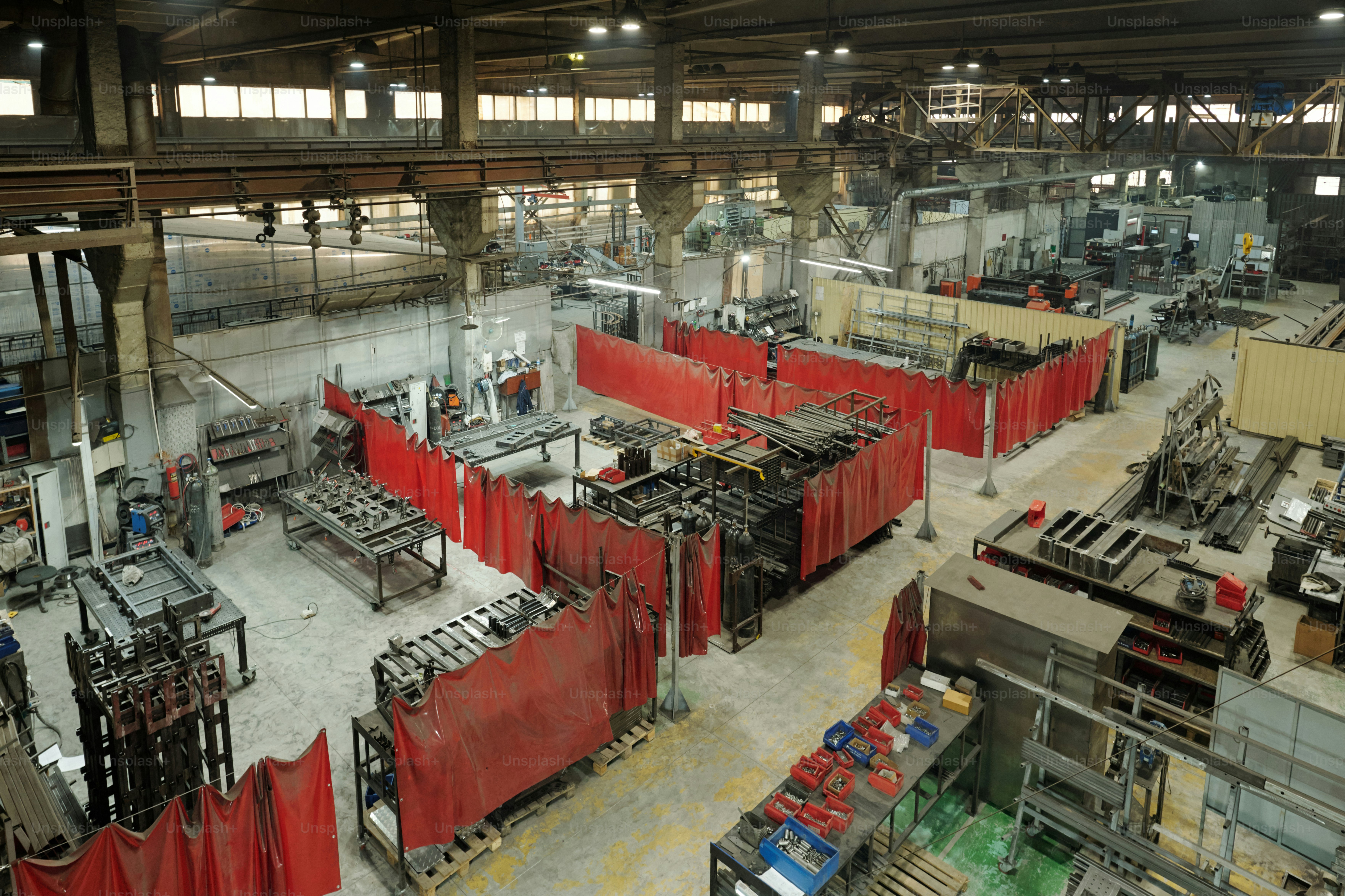 Red curtains dividing several workshops with machines or parts of warehouse with huge metallic spare parts from each other