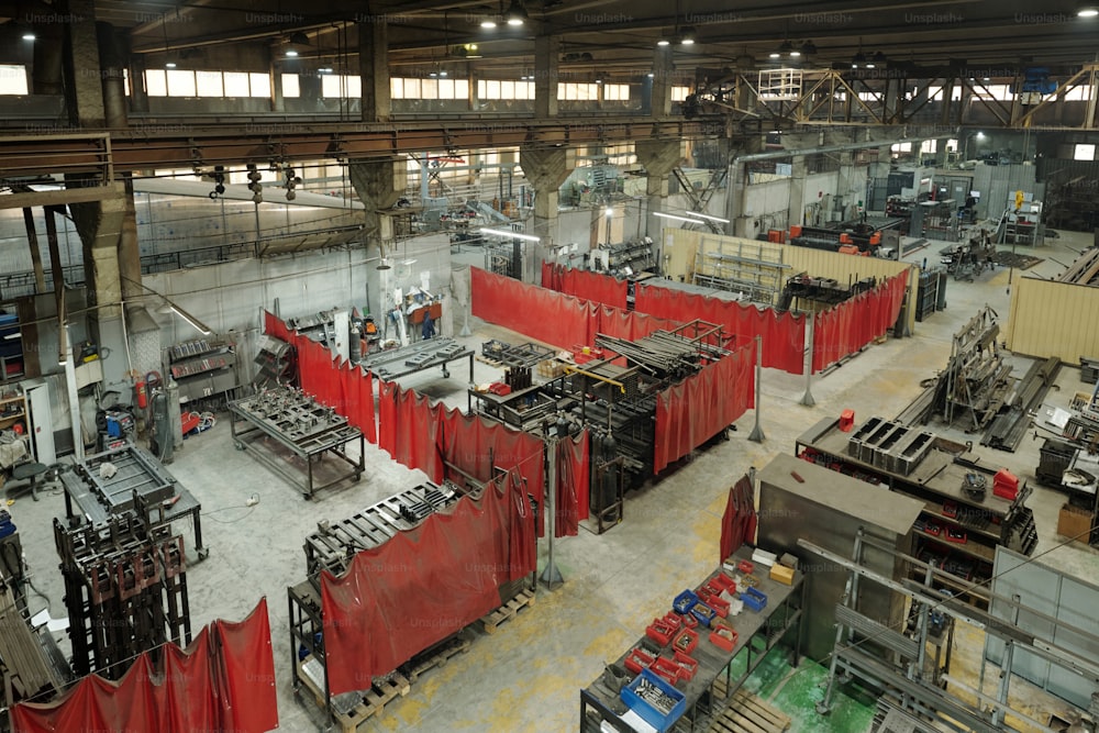 Red curtains dividing several workshops with machines or parts of warehouse with huge metallic spare parts from each other