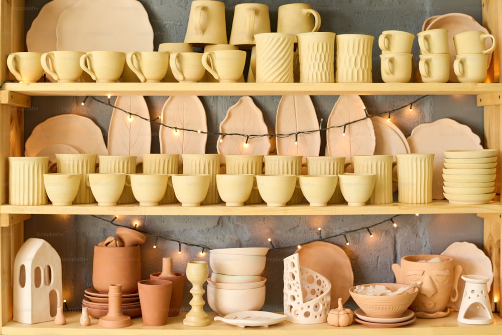 Large display with variety of handmade earthenware and clay items such as mugs, bowls, pots and plates for sale in small shop of handcraft