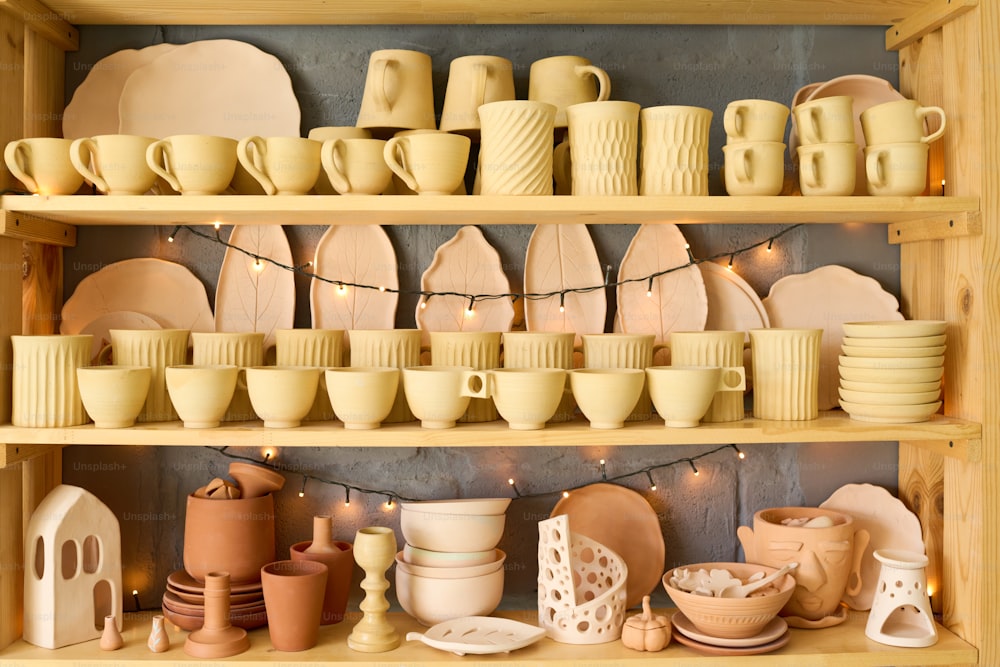 Large display consisting of three shelves with handmade clay products such as mugs, cups, plates, bowls, pots and vases in shop
