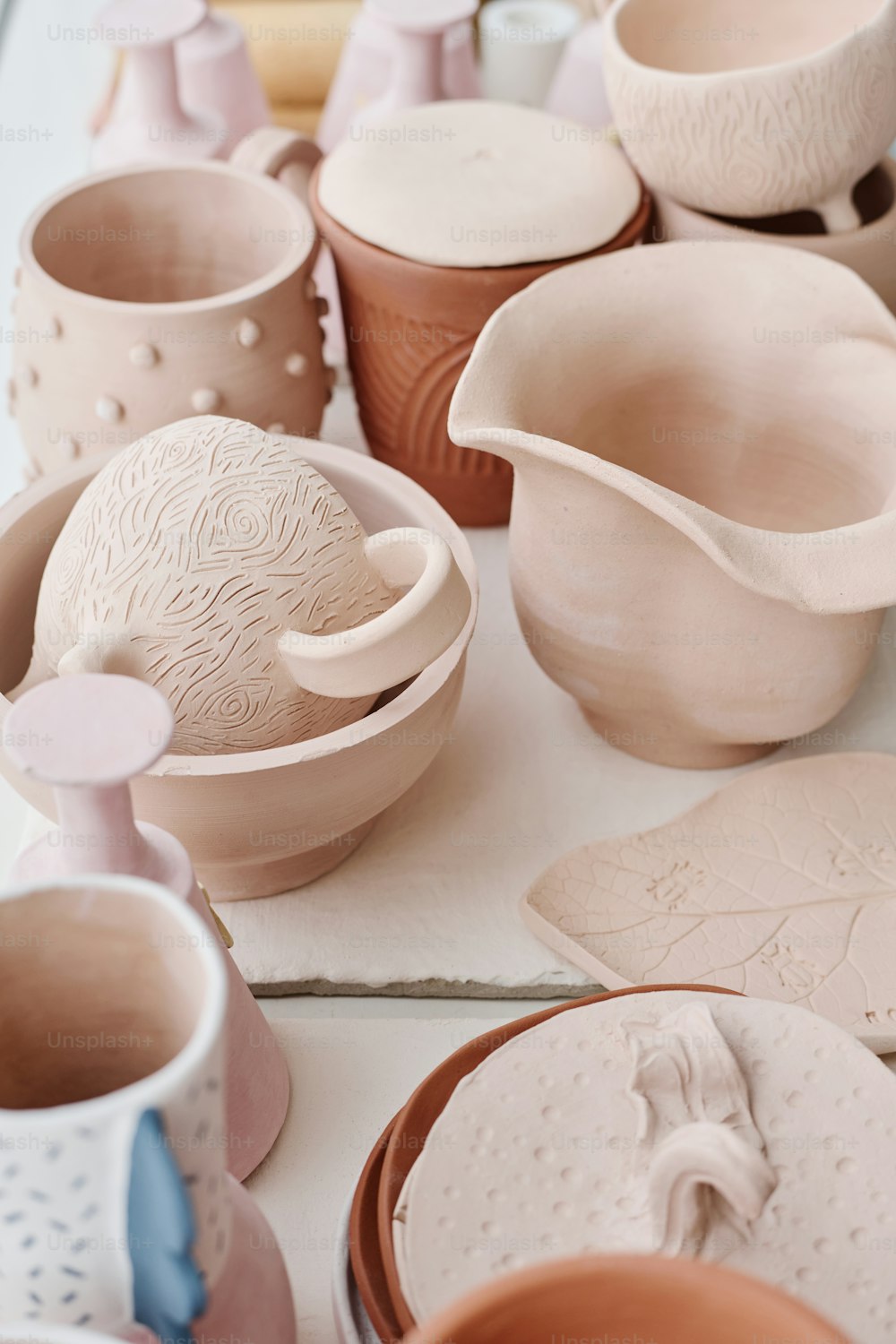Assortment of handmade earthenware such as bowls, cups, mugs, jugs, pots and other kinds of clay items on display or table in workshop