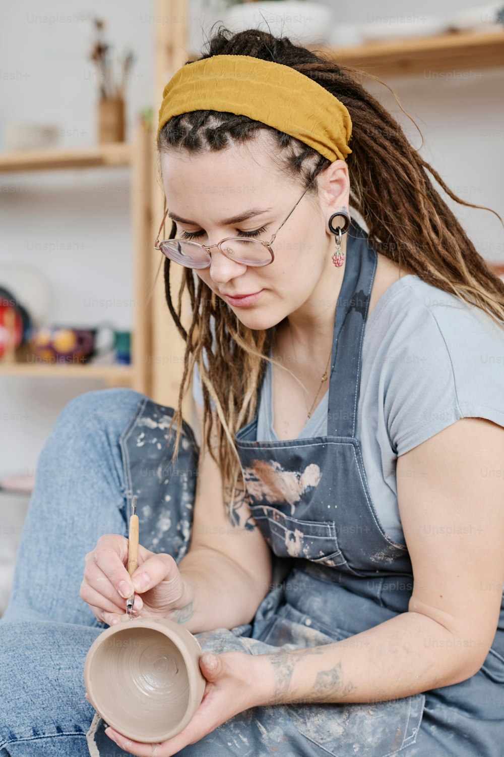 Oleiro feminino criativo jovem no ornamento de escultura casualwear nos lados do item de argila artesanal enquanto trabalha sobre a criação de barro