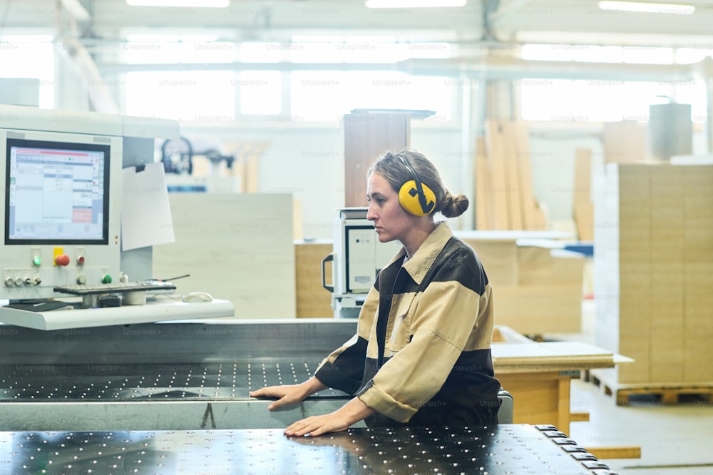 Joven trabajadora con auriculares protectores de pie junto a la máquina en la planta