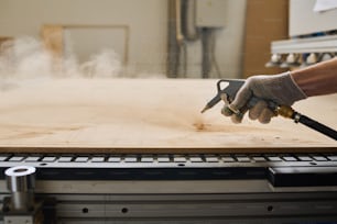Close-up of worker in gloves processing wooden board with special equipment at machine