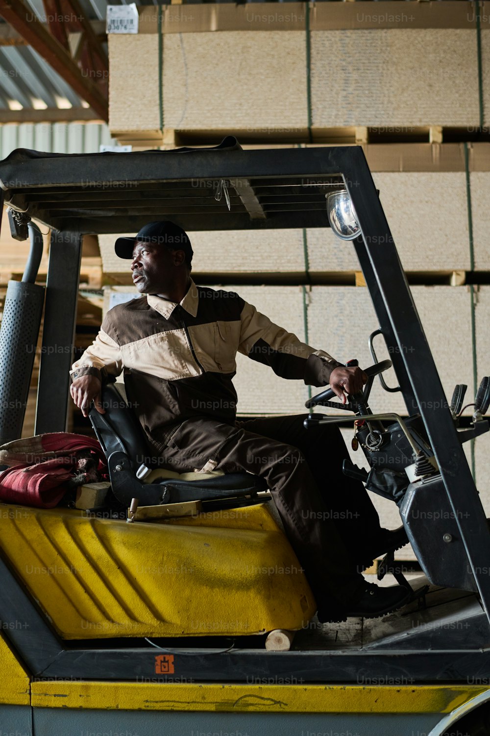 Conducteur de chariot élévateur africain assis dans une chargeuse et conduisant pendant le travail dans une usine industrielle