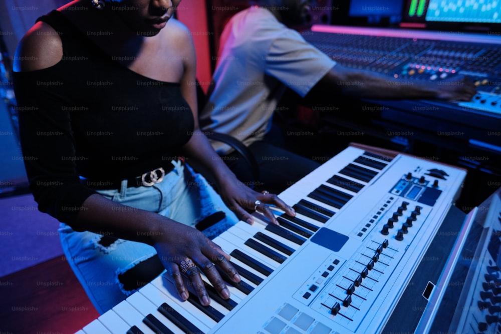 Mujer afroamericana tocando el teclado digital mientras el productor musical trabaja en el mezclador en el estudio de grabación, iluminación de neón