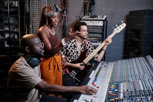 Produtor musical afro-americano maduro, jovem cantora e guitarrista masculino trabalhando na música em estúdio de gravação