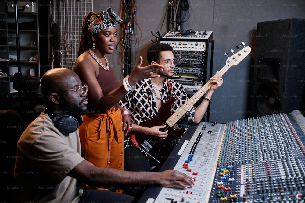 成熟したアフリカ系アメリカ人の音楽プロデューサー、若い女性歌手、レコーディングスタジオで曲に取り組んでいる男性ギタリスト