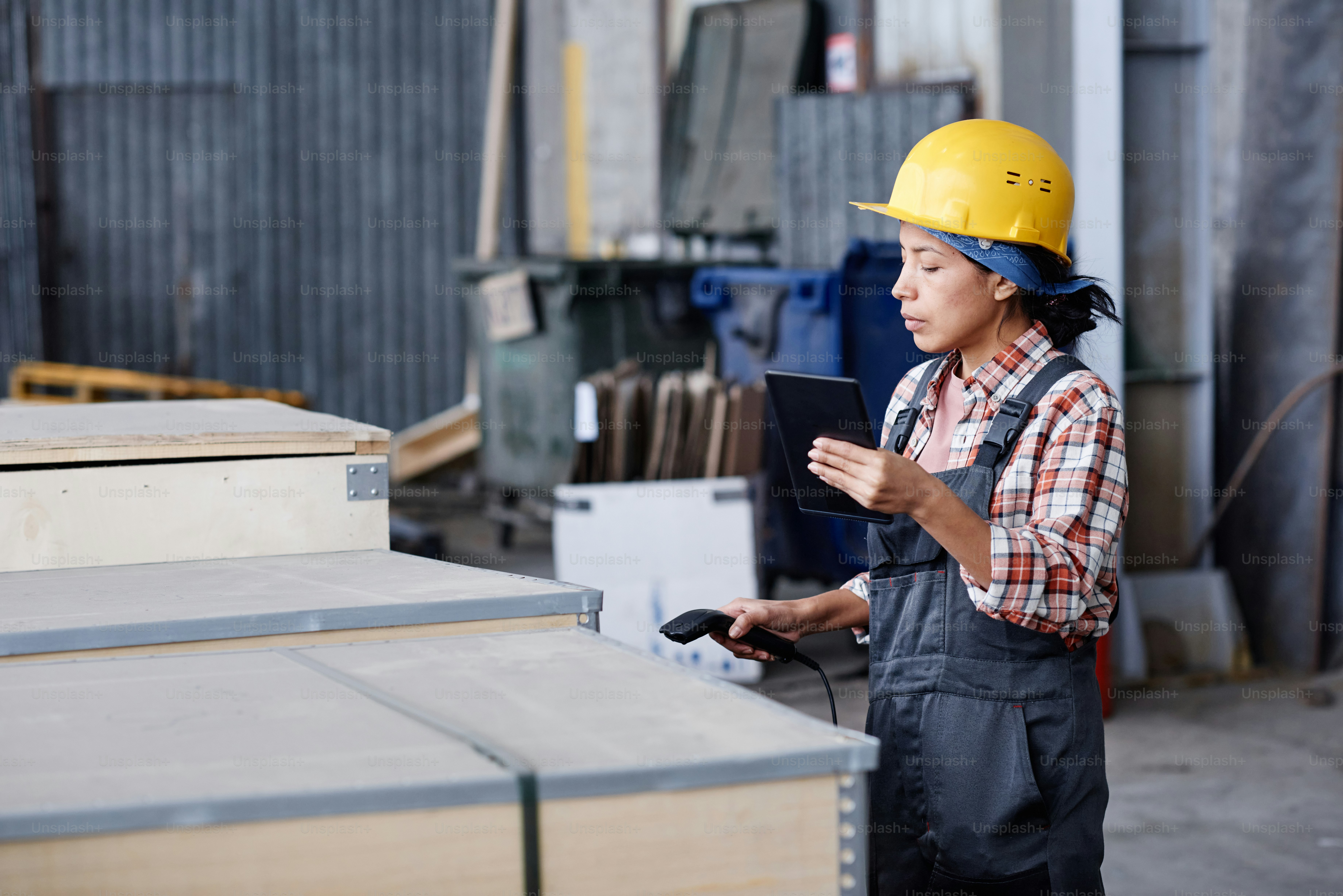 Young female worker of distribution warehouse scanning code on container with new equipment or spare parts for machines