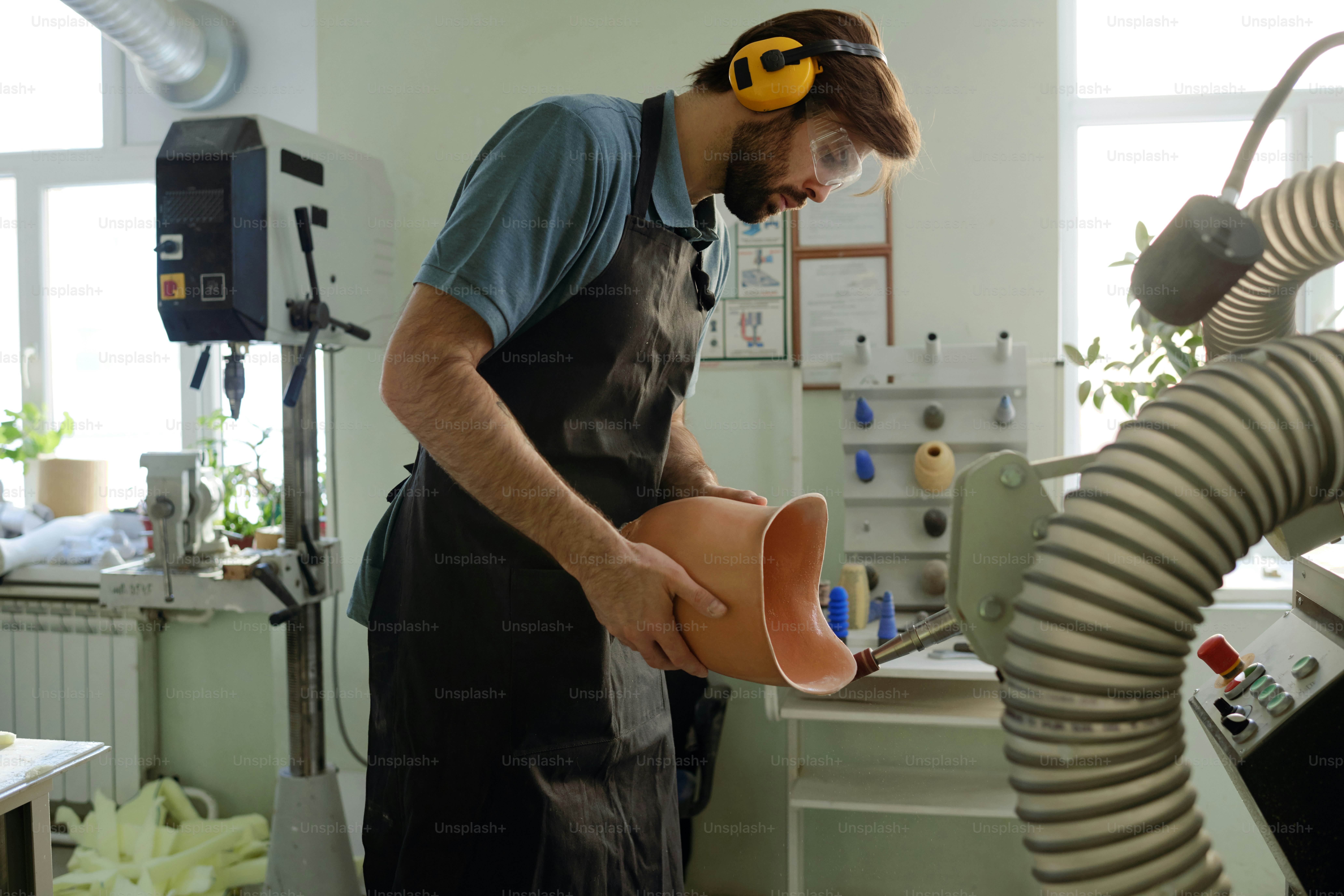 Junger Mann in schützender Arbeitskleidung, der die Kanten der Silikonauskleidung, die Teil des Prothesenschaftes ist, in der Fabrikwerkstatt glättet