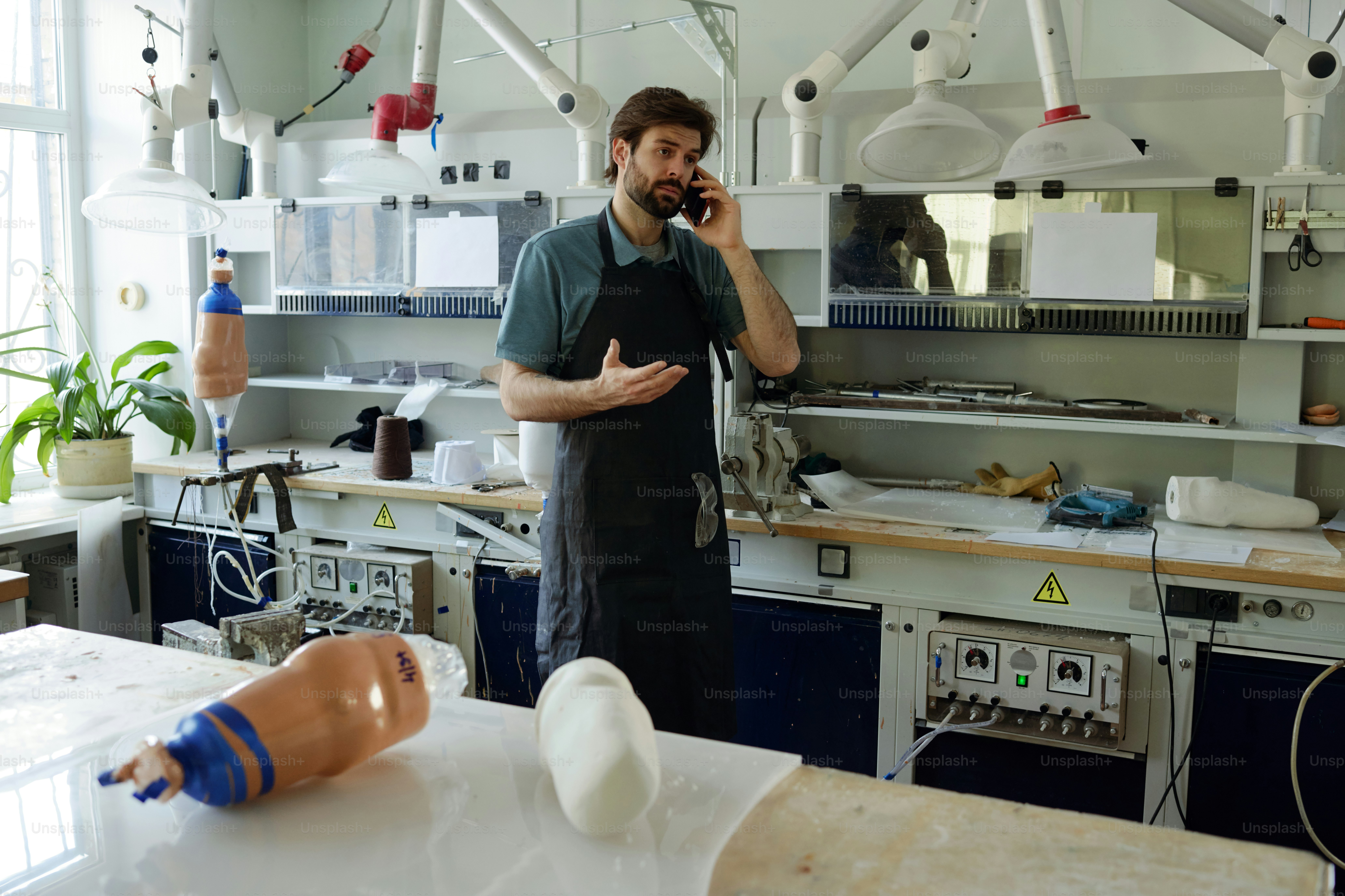 Junger vielbeschäftigter Arbeiter der Manufaktur, der mit dem Kunden auf dem Handy spricht und gleichzeitig über die Bereitschaft der Prothese berät