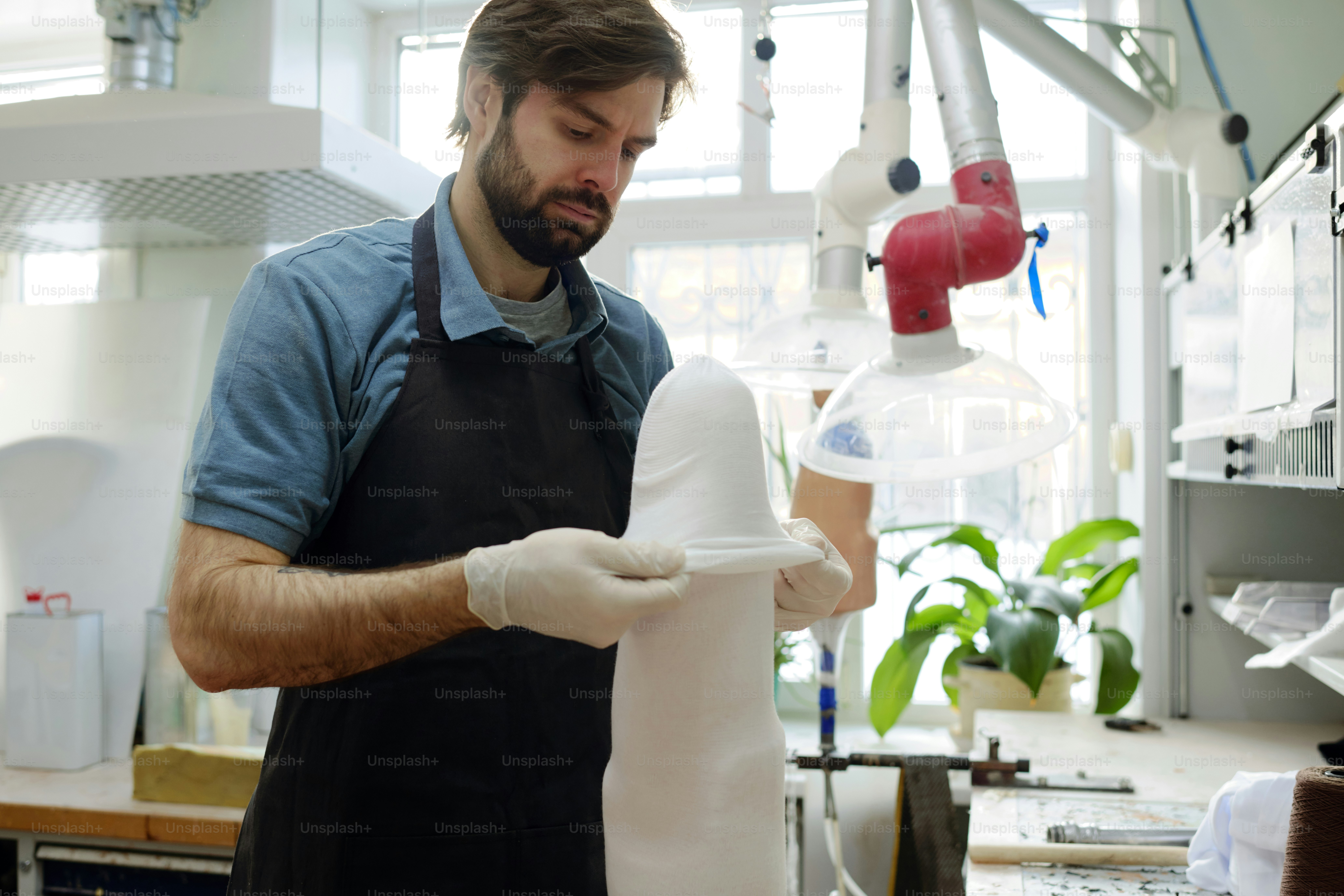 Junger ernster Mann in Schürze und Handschuhen, der thermoplastische Folie über den gesamten Prothesenschaft legt, während er an einem der Kundenaufträge arbeitet