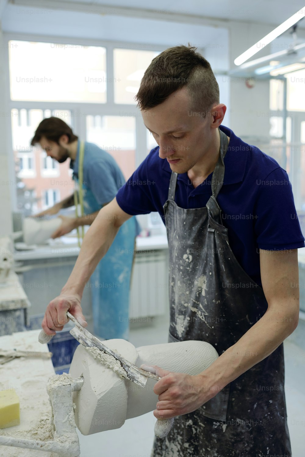 Worker of prosthetic factory cutting upper part of plaster cast while forming shape of residual limb against colleague