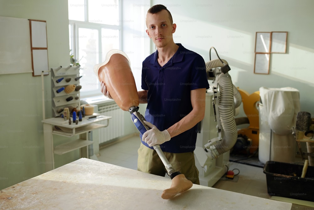 Giovane specialista della manifattura che tiene protesi di gamba pronta composta da presa protesica, meccanismo metallico e piede