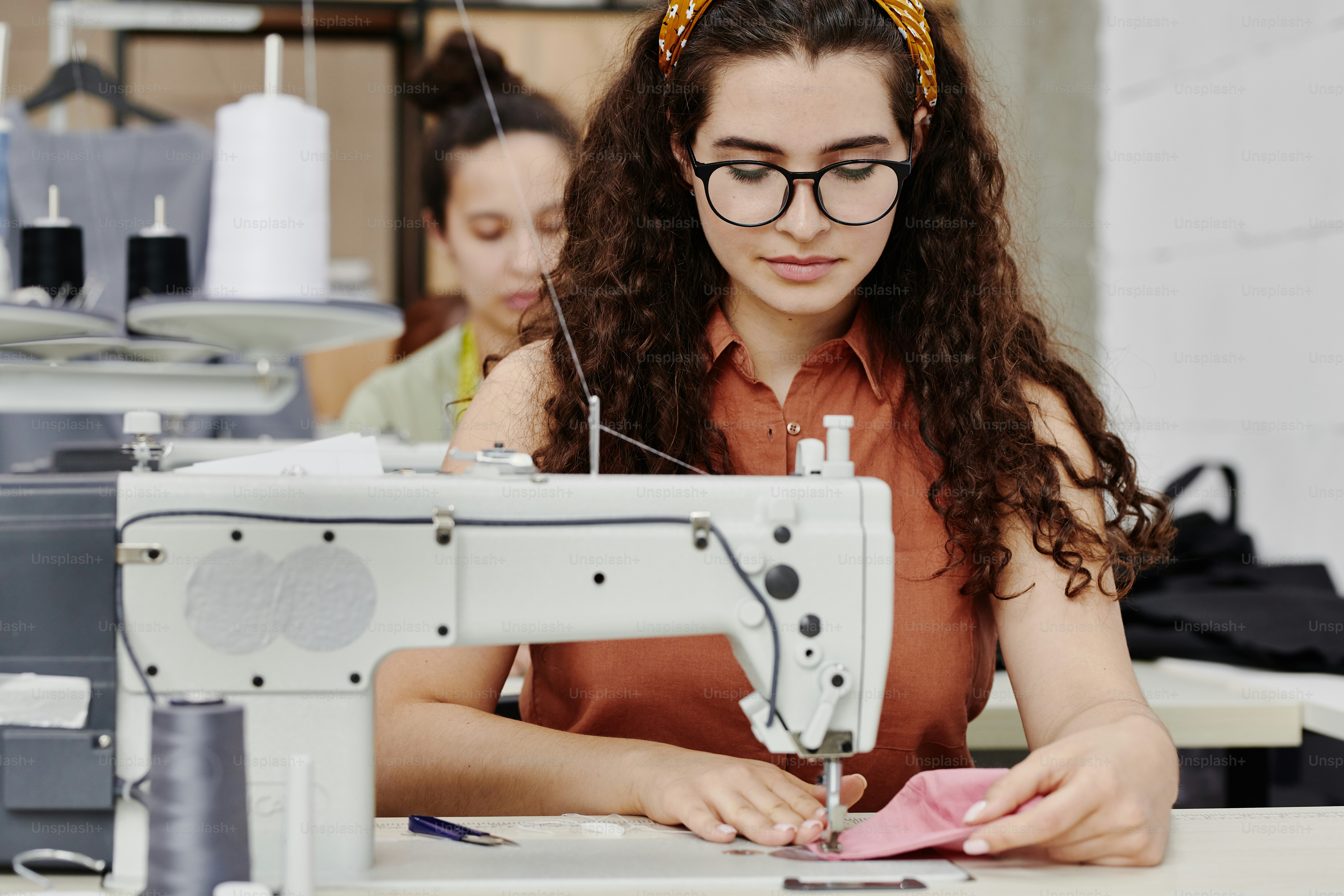 Giovane sarta seria seduta dalla macchina da cucire elettrica mentre fa spalline per nuovi vestiti, cappotti o altri articoli di abbigliamento