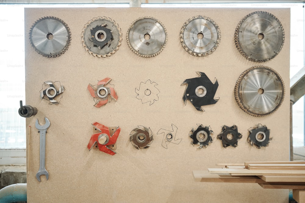 Large square toolboard with metallic wrench, group of details for electric circle saw and stack of long narrow wooden boards in workshop