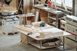 Workbench of furniture factory worker with wooden workpieces, electric handtools and other stuff surrounded by various equipment