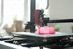 Cabezal de impresión de la impresora 3D moviéndose sobre la base del objeto redondo rosa en la capa de trabajo durante el proceso de impresión