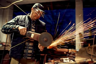 Craftsman sawing metal. Grinder making hot sparkles all around.