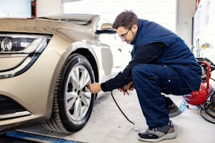 Un mécanicien automobile gonfle le pneu de la voiture à l’atelier du mécanicien.