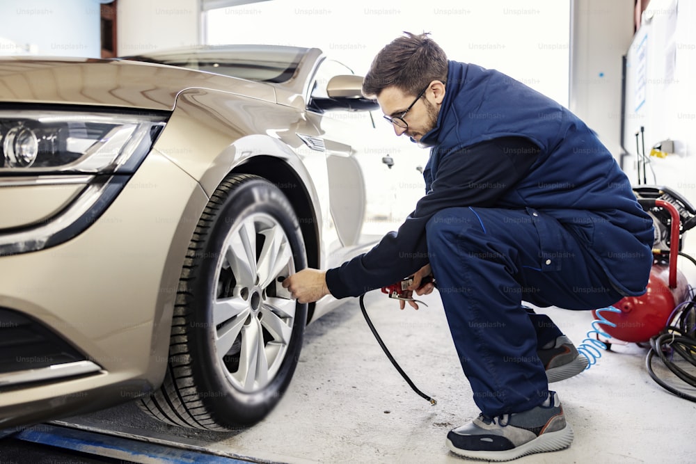 An auto mechanic inflates the car tire at mechanic's workshop.