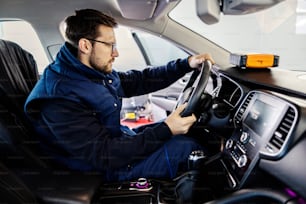 An auto mechanic sitting in a car and testing steering wheel at mechanic's shop.