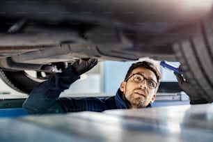 An expert for cars examining car in mechanic's pit.