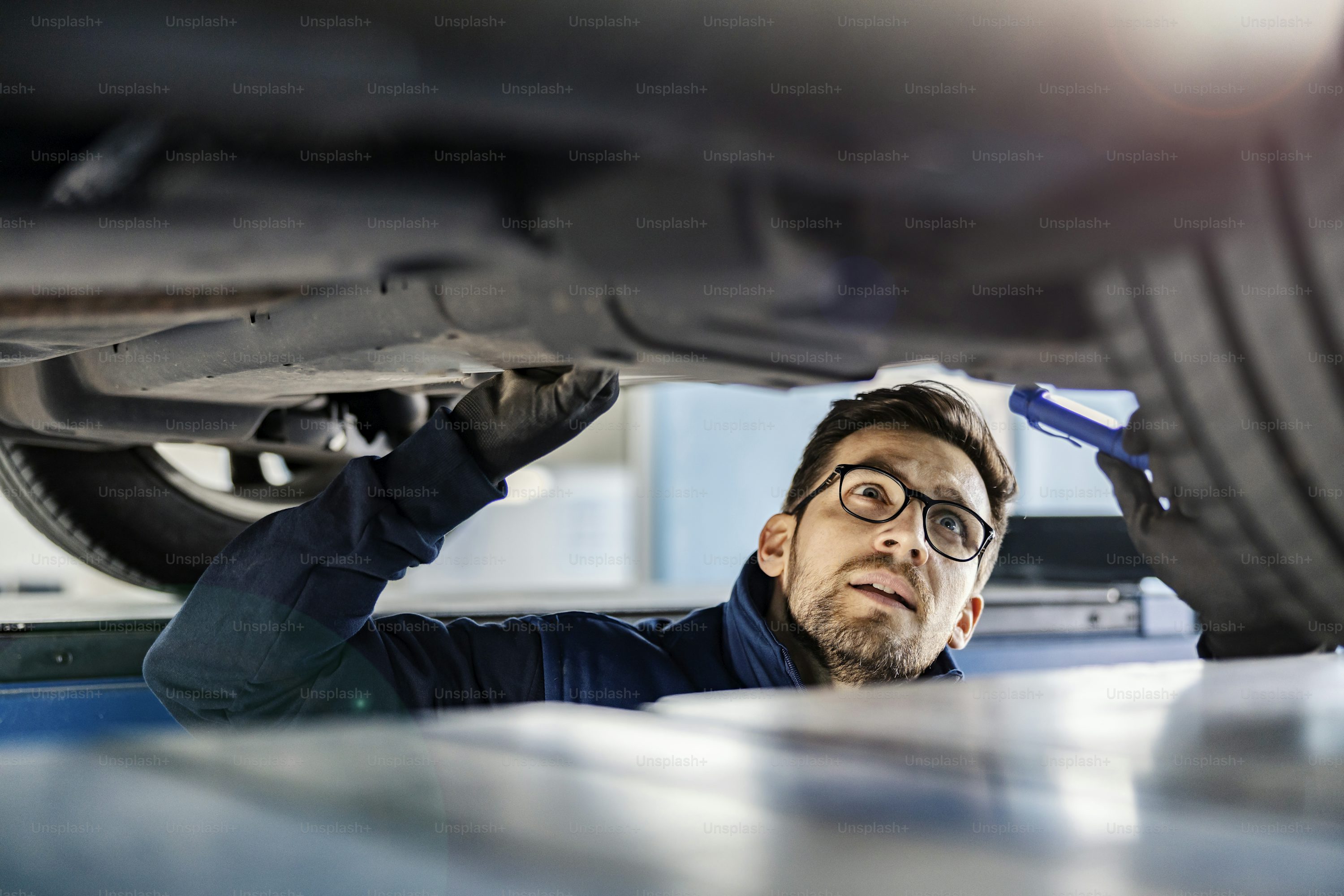 An expert for cars examining car in mechanic's pit.