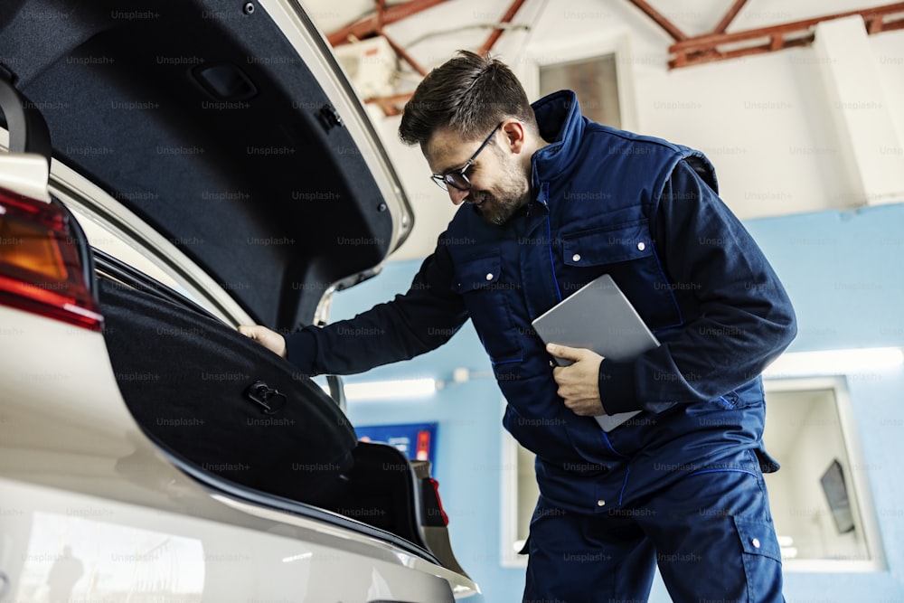 A worker with tablet does technical inspection at mechanic's shop.