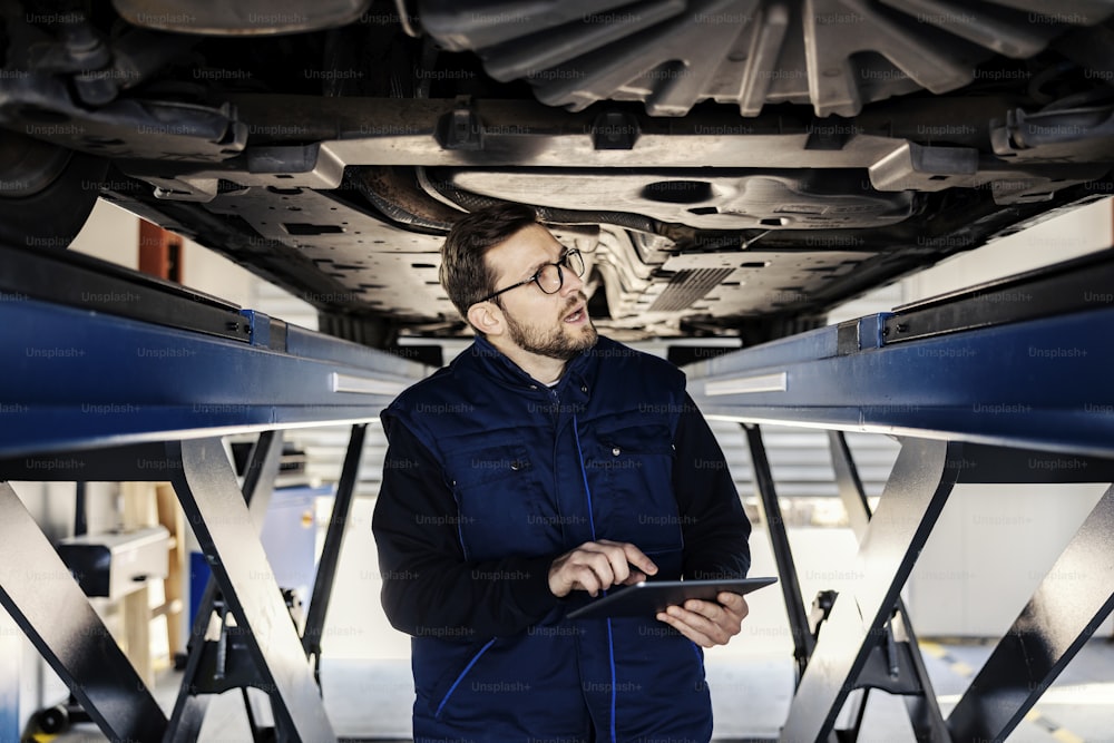 A focused technician with tablet looks under the car.