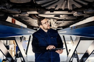 Un tecnico concentrato con tablet guarda sotto l'auto.