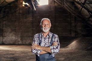 A proud senior worker standing in the warehouse with arms crossed and looking at the camera. In the background are sugar beet products. Senior factory worker standing in the warehouse.