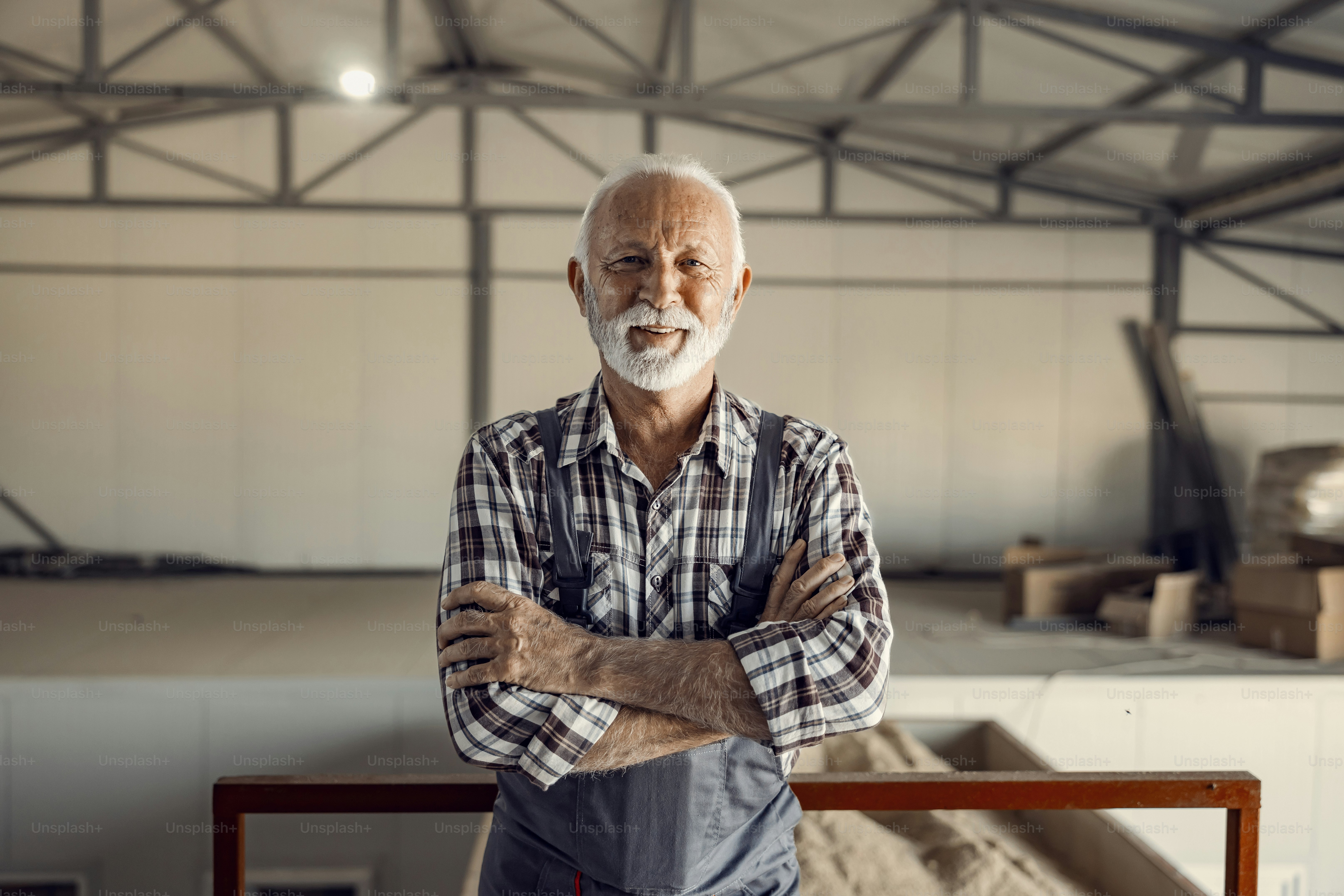 Exitosos trabajadores senior de fábrica. Un orgulloso y sonriente trabajador de la fábrica en uniforme de trabajo está de pie en la fábrica con los brazos cruzados.