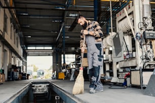 A worker sweeping dust from the floor with broom in a mechanic's shop.