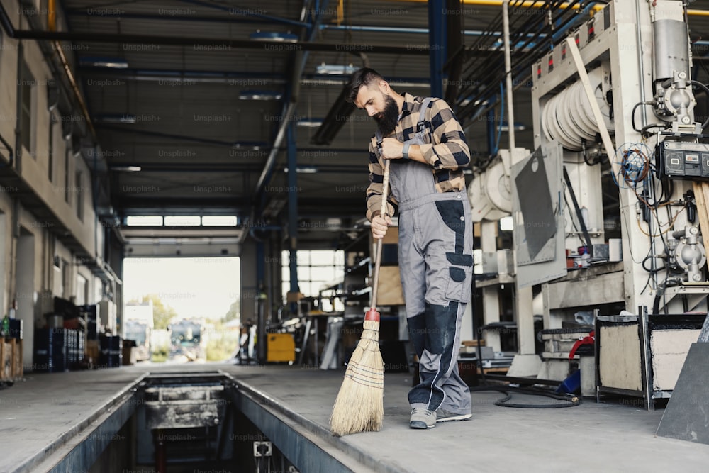Um trabalhador varrendo a poeira do chão com vassoura em uma oficina mecânica.