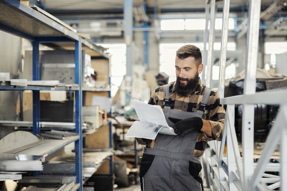 A car industry worker leaning on the bus construction and checks paperwork in workshop.