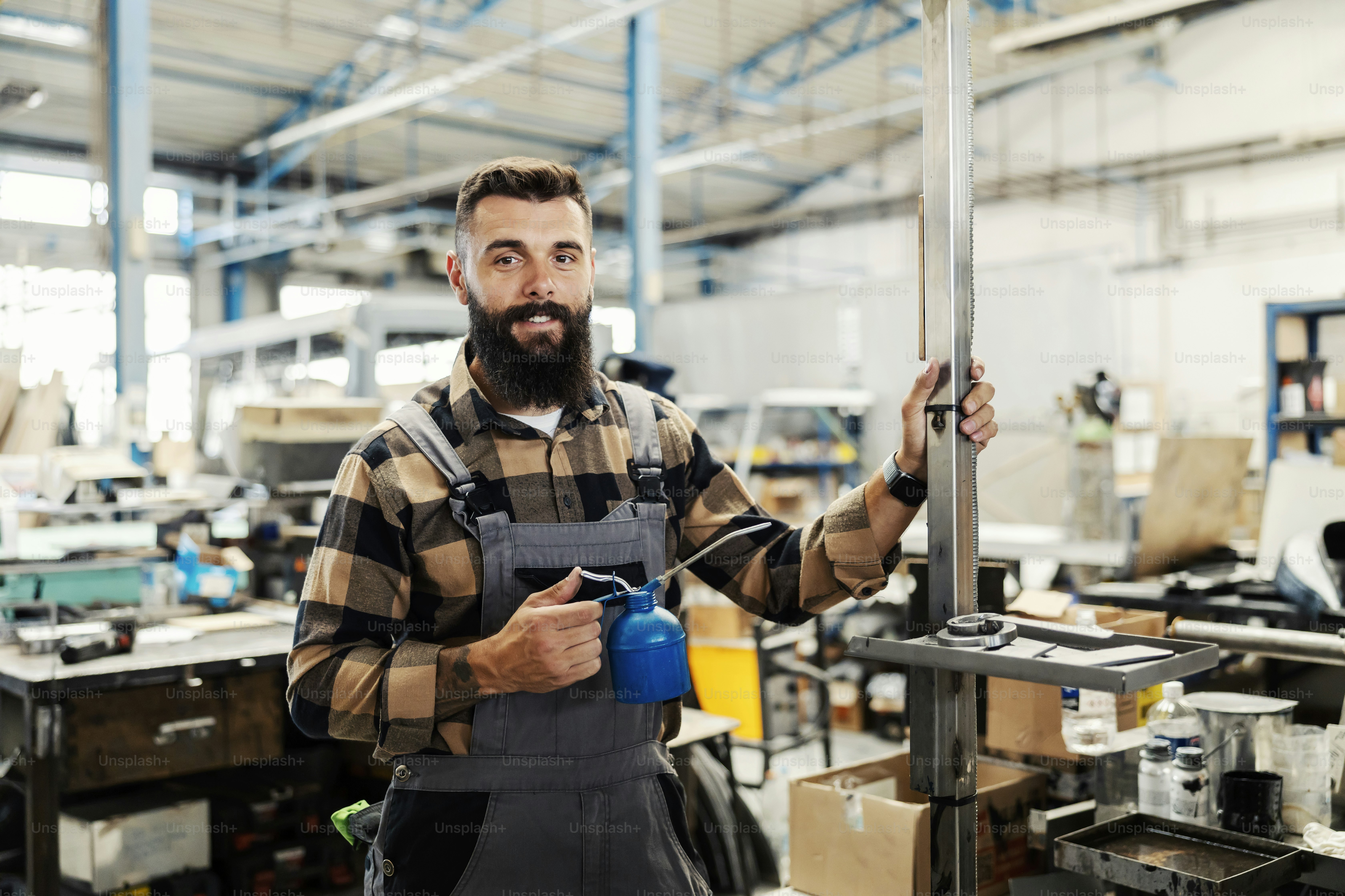 A heavy industry worker with oil can in hands smiling at the camera while working.