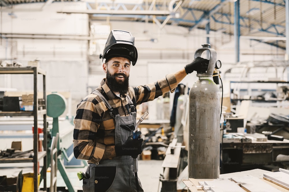 A heavy industry worker posing with welding machine in facility.