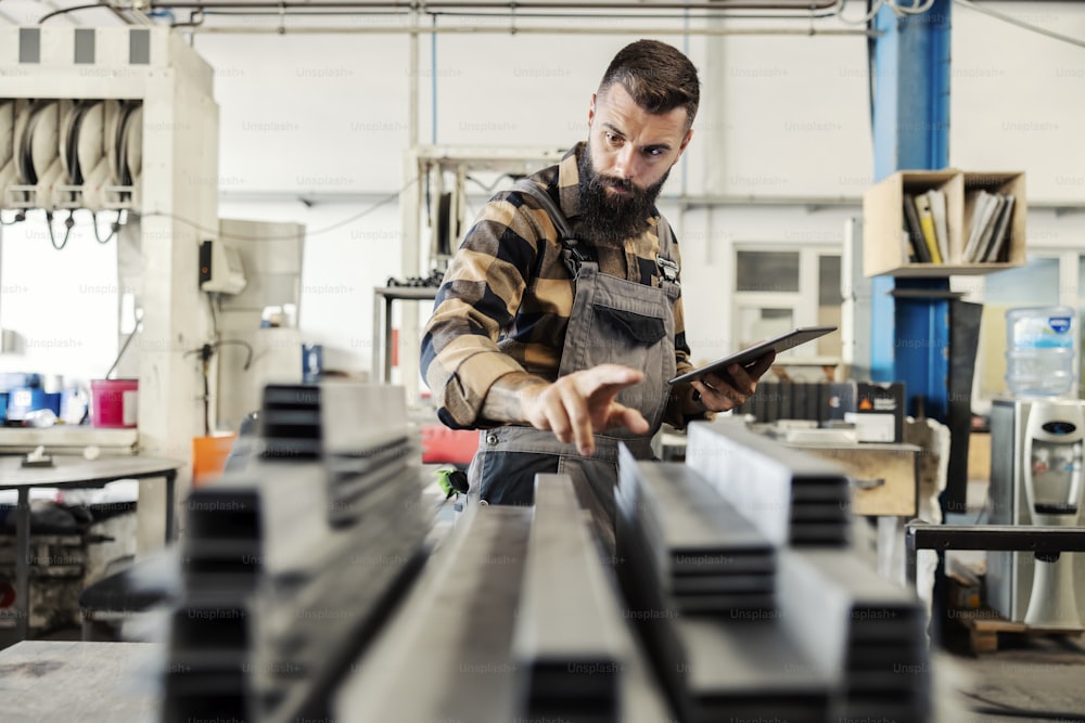 A heavy industry worker checking on inventory with tablet in workshop.