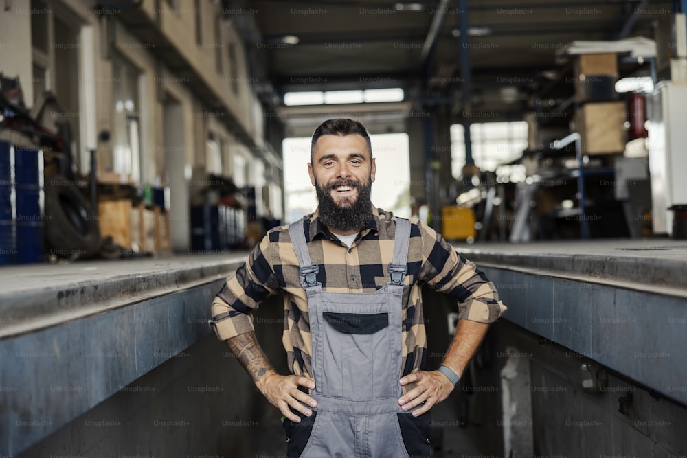 A smiling auto mechanic proudly standing in mechanic's pit and looking at the camera.