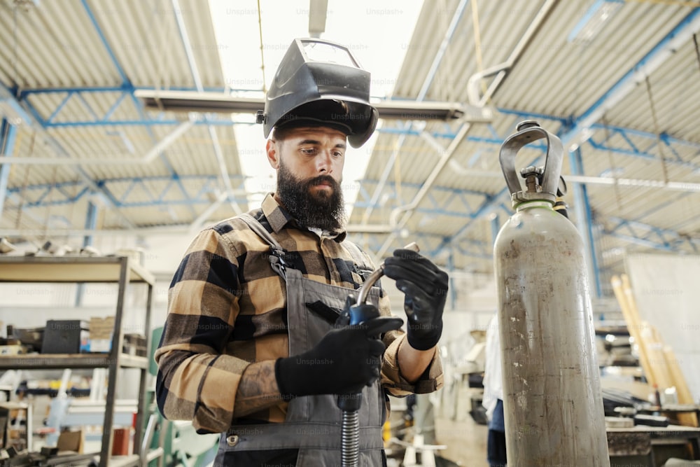 A metallurgy worker adjusting welder and preparing it for work in factory.
