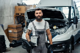 A mechanic holding tools and equipment and smiling at the camera.