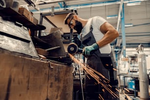 Ein Arbeiter, der Metall mit einer Schleifmaschine in der Werkstatt schneidet.