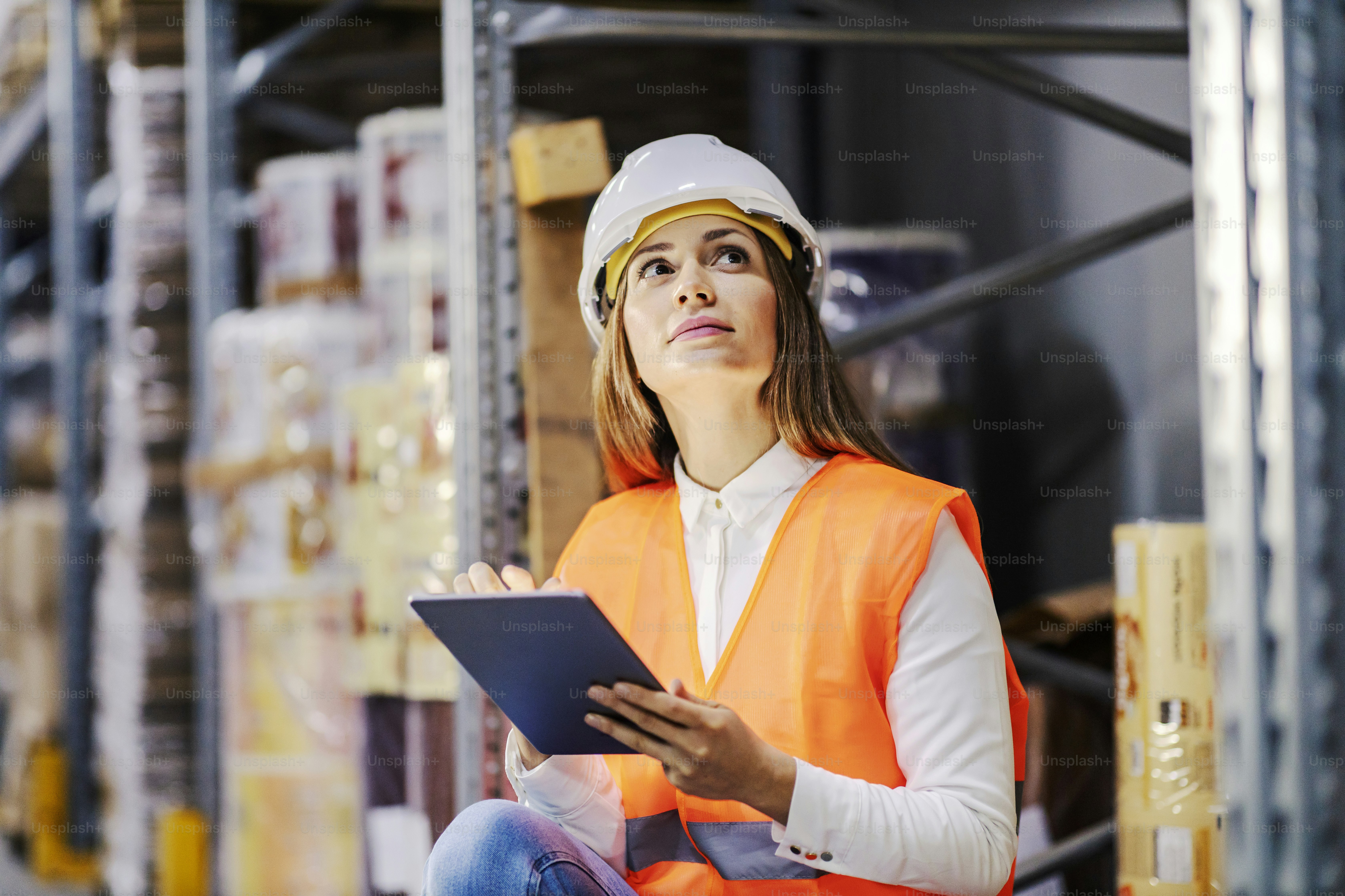 A factory storage manager is sitting and adding orders for shipment on tablet.