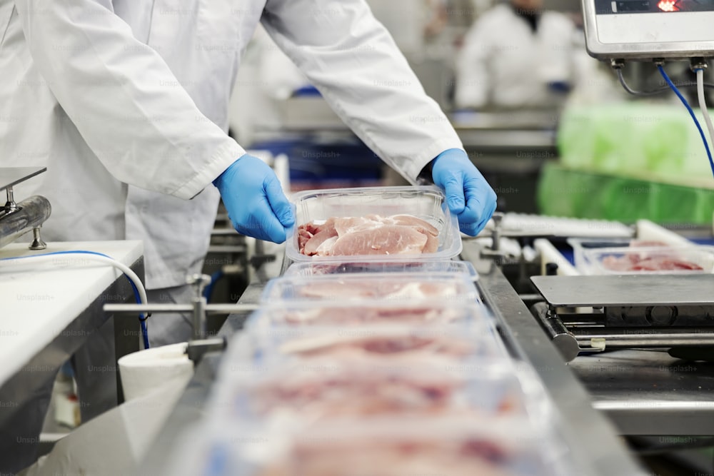 Close up of a meat industry worker gathering packed meat on a conveyor belt.