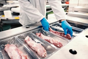 Primo piano di un operaio di una fabbrica alimentare che confeziona la carne nella plastica su una macchina per l'imballaggio. Spesa di una carne.