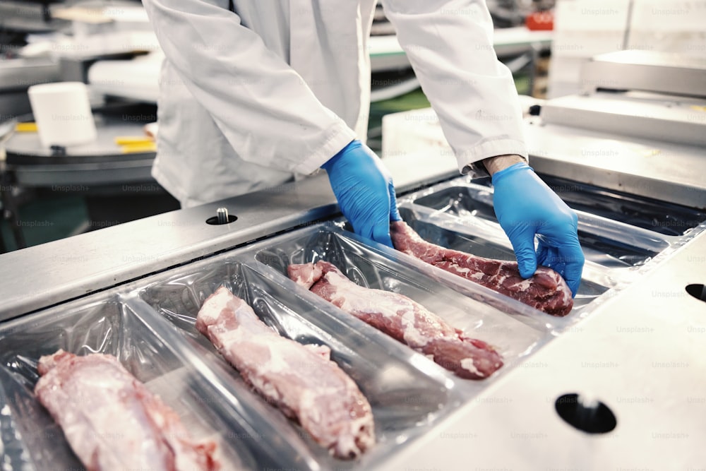 Nahaufnahme eines Arbeiters in einer Lebensmittelfabrik, der Fleisch auf einer Verpackungsmaschine in den Kunststoff packt. Kosten für ein Fleisch.